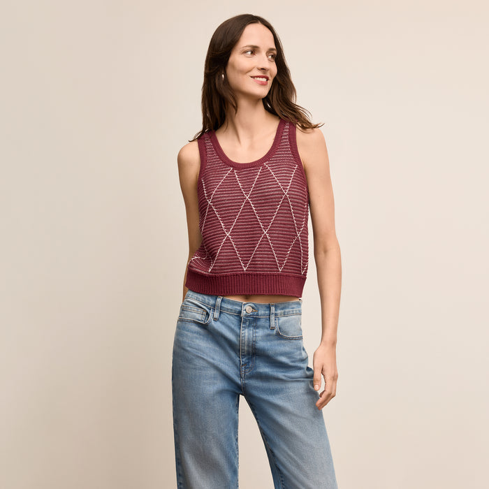 Woman wearing a maroon sleeveless knitted top and blue jeans on a beige background | Lead