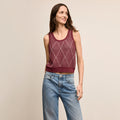 Woman wearing a maroon sleeveless knitted top and blue jeans on a beige background | Lead