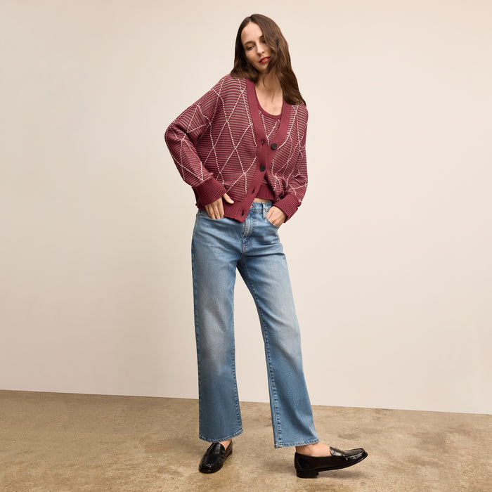 Woman wearing a patterned sweater and blue jeans against a plain background