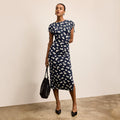 Woman wearing a navy dress with white floral pattern against a beige background | Lead