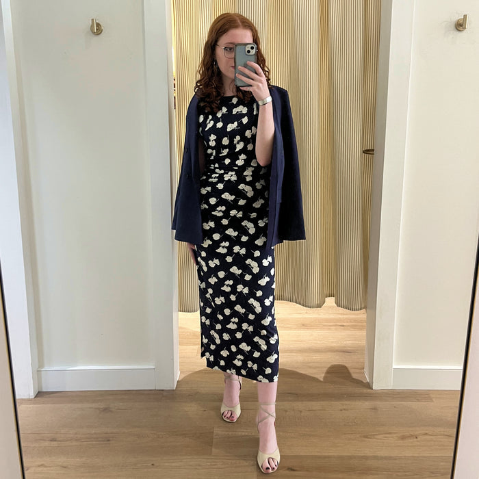 Woman taking a mirror selfie wearing a navy dress with white floral pattern and navy cardigan.