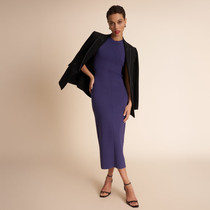 Woman wearing a purple dress with a black jacket on a beige background