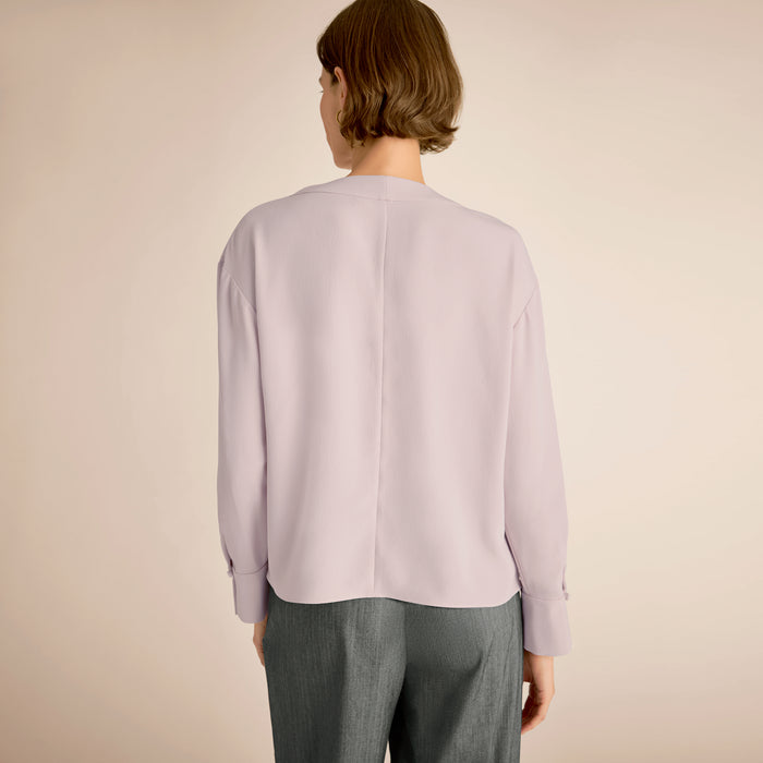 Person wearing a light purple cardigan and gray pants on a beige background
