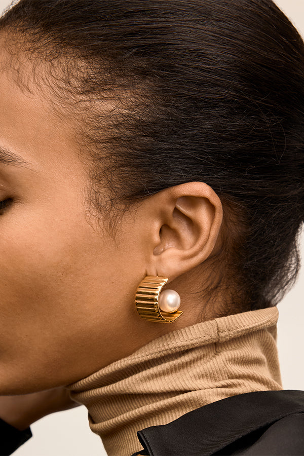 Close-up of a person wearing a gold earring with a pearl accent. | Exclude | Grid Hover