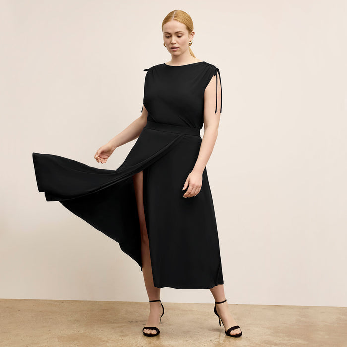 Woman wearing a black dress with a slit on a beige background