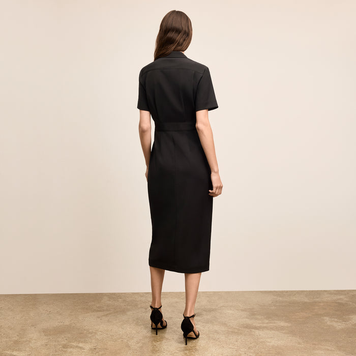 Woman wearing a black dress standing against a beige background
