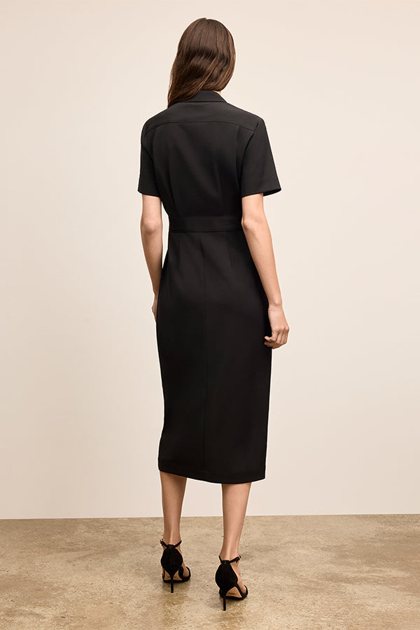 Woman wearing a black dress standing against a beige wall. | Exclude | Grid Hover