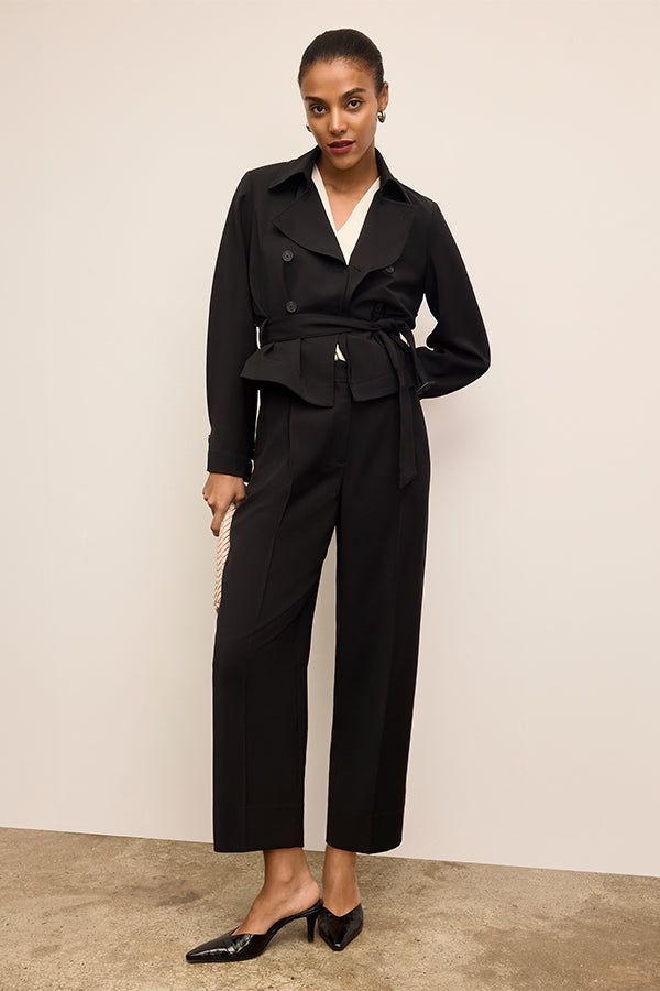 Woman wearing a black suit with a white shirt against a beige background | Exclude