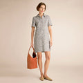 Woman wearing a checkered dress holding an orange bag on a beige background | Lead