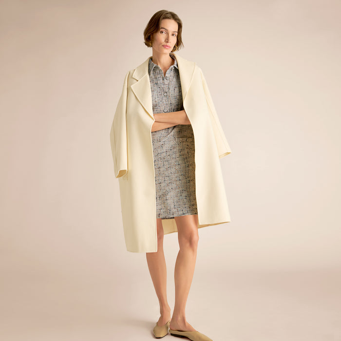 Woman wearing a light-colored coat over a dress on a beige background. | Exclude