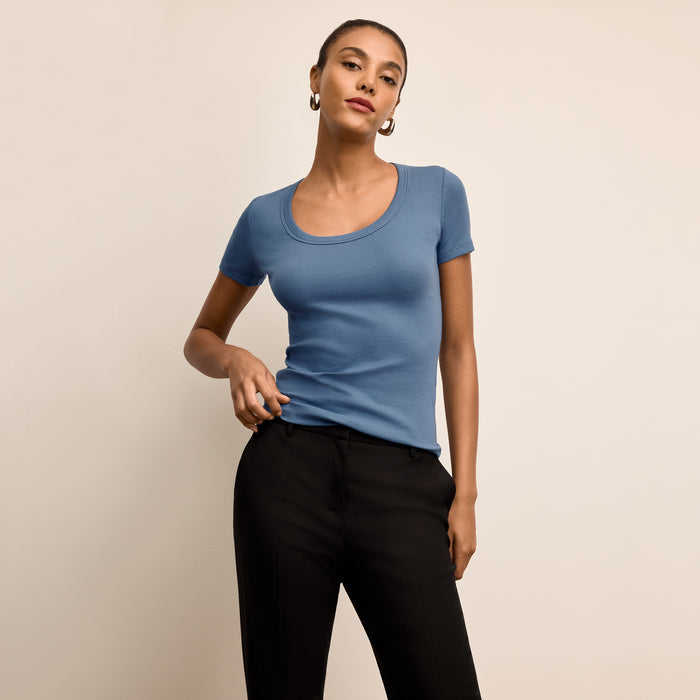 Woman wearing a blue t-shirt and black pants against a beige background | Lead