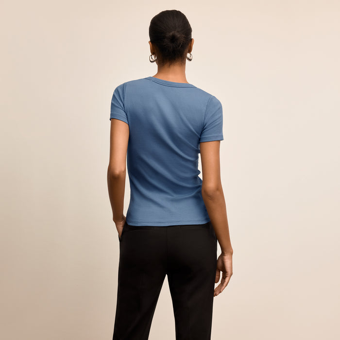 Person wearing a blue t-shirt and black pants on a beige background