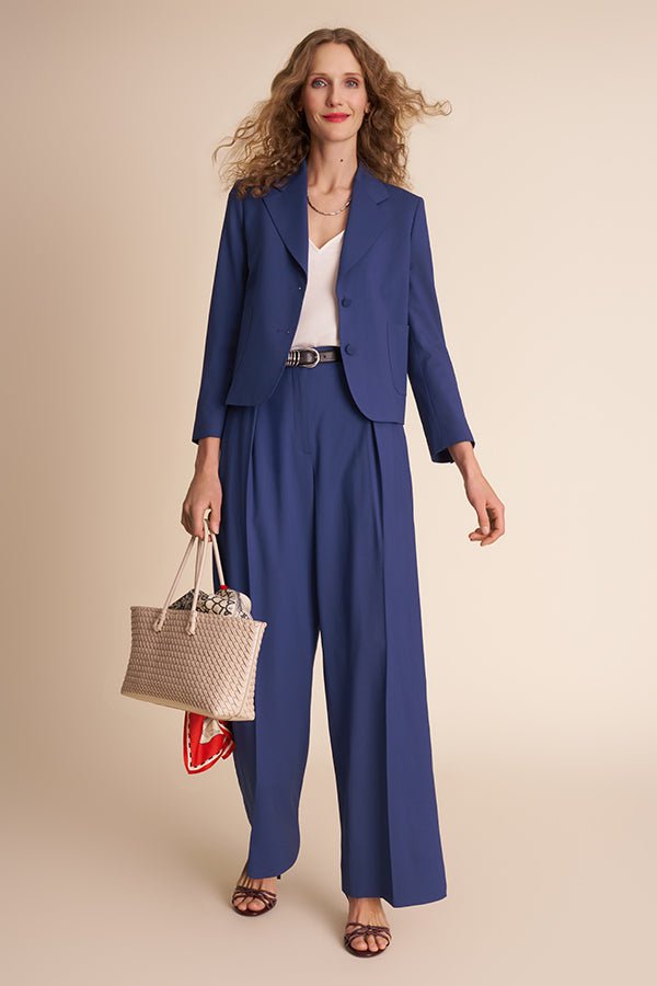 Woman wearing a blue suit holding a woven handbag on a beige background | Exclude