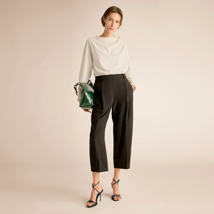 Woman wearing a white top and black pants holding a green handbag on a beige background