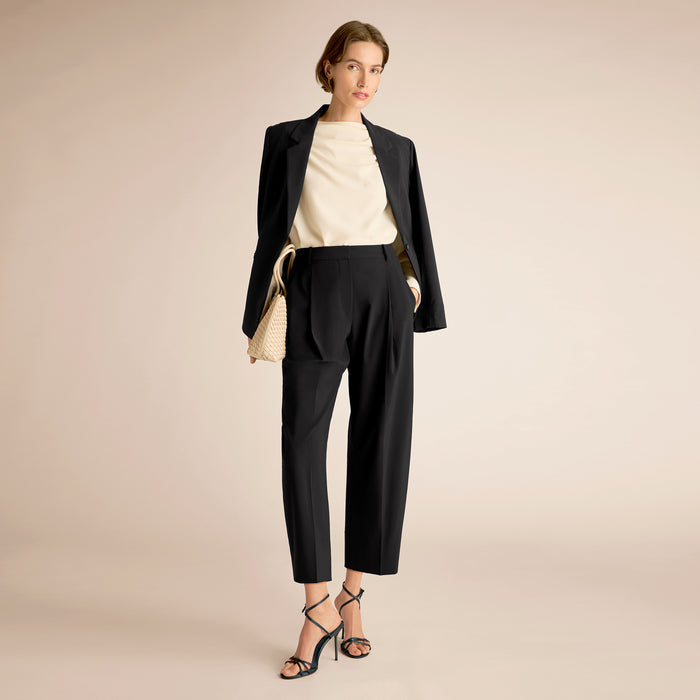 Woman wearing a black suit with a beige top on a beige background