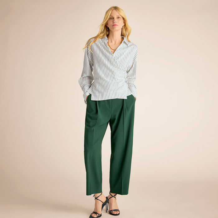 Woman wearing a striped shirt and green pants on a beige background