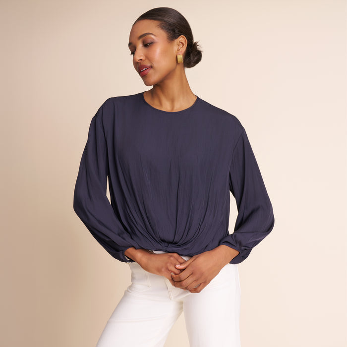 Woman wearing a dark blue long-sleeve top and white pants on a beige background | Lead