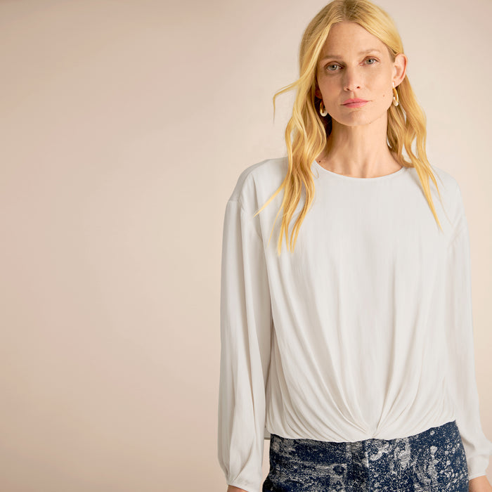 Woman wearing a light gray long-sleeve top against a beige background | Lead