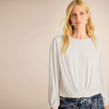 Woman wearing a light gray long-sleeve top against a beige background | Lead