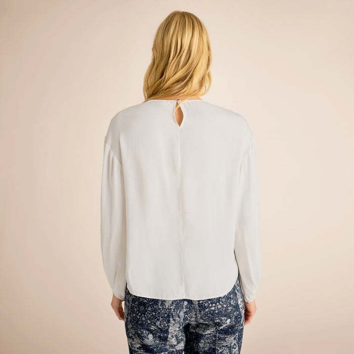 Person wearing a white blouse with a beige background