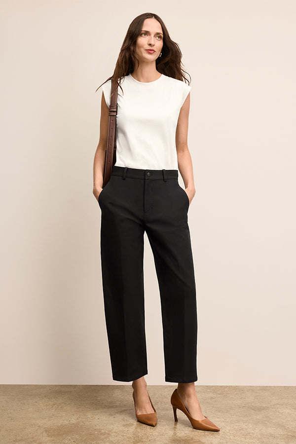 Woman wearing a white sleeveless top and black high-waisted pants against a beige background | Exclude