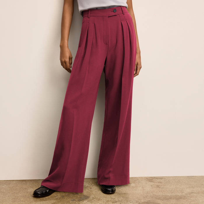 Person wearing maroon wide-leg pants against a beige wall. | Lead