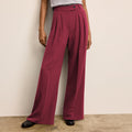 Person wearing maroon wide-leg pants against a beige wall. | Lead