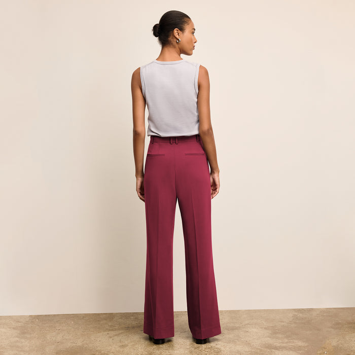 Woman wearing a white sleeveless top and maroon high-waisted pants on a beige background
