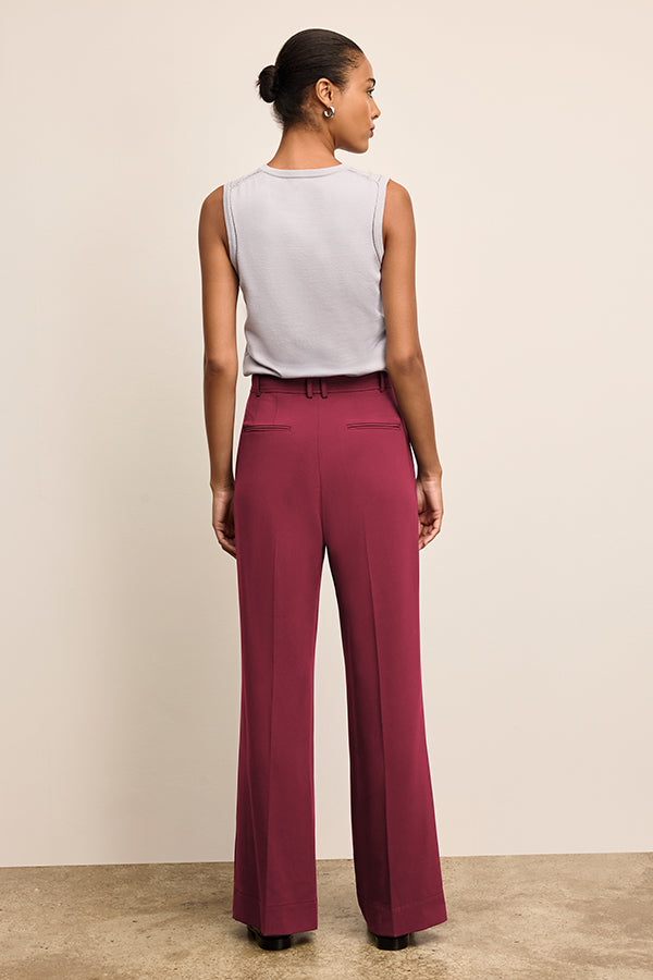 Woman wearing a sleeveless white top and burgundy pants against a beige background | Exclude