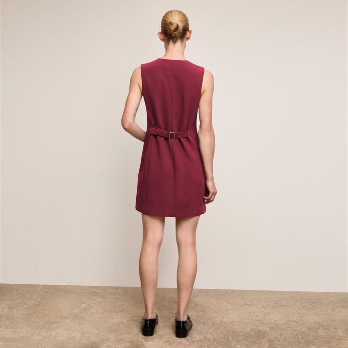Woman wearing a burgundy dress with a belt on a plain background