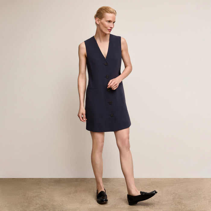 Woman wearing a navy sleeveless dress against a beige background | Lead