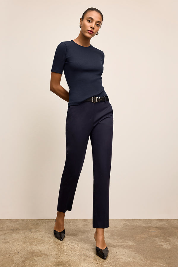 Woman wearing a navy blue top and pants with a belt against a beige background | Exclude | Grid