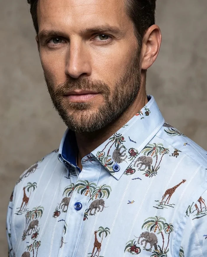 Man wearing a patterned shirt with animals and plants on a neutral background
