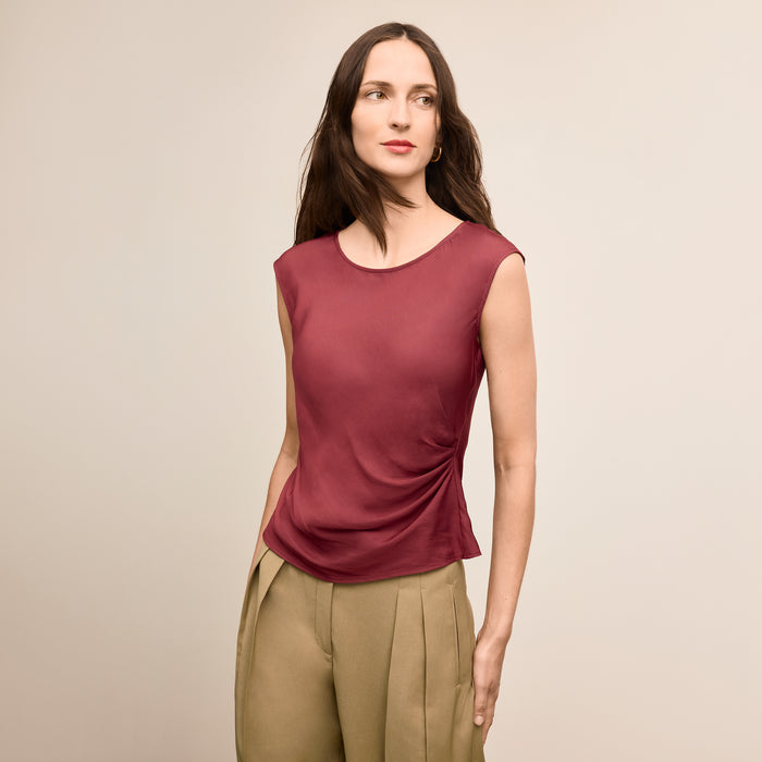 Woman wearing a maroon sleeveless top and beige pants against a beige background | Lead
