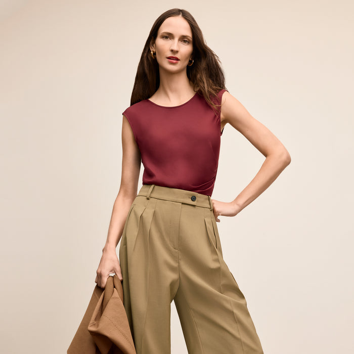 Woman wearing a burgundy top and beige pants against a beige background