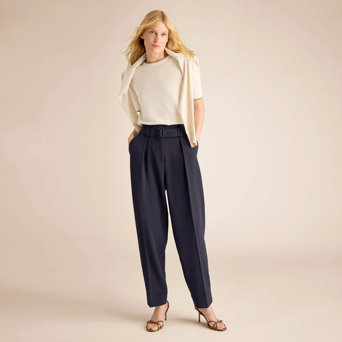 Woman wearing a white top, beige cardigan, and navy pants on a beige background