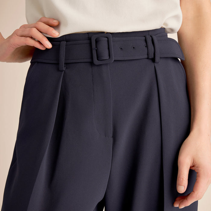 Navy pleated pants with a belt on a neutral background