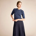 Woman wearing a navy sweater with white polka dots and a matching skirt on a beige background | Lead