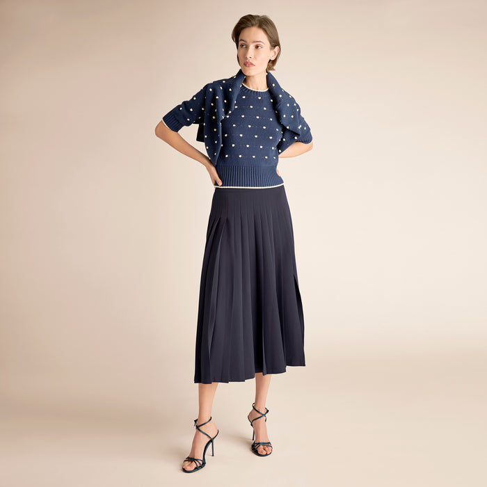 Woman wearing a navy polka dot sweater and skirt on a beige background