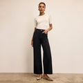 Woman wearing a white top and black pants against a beige background | Lead