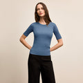 Woman wearing a blue short-sleeve top and black pants on a beige background | Lead