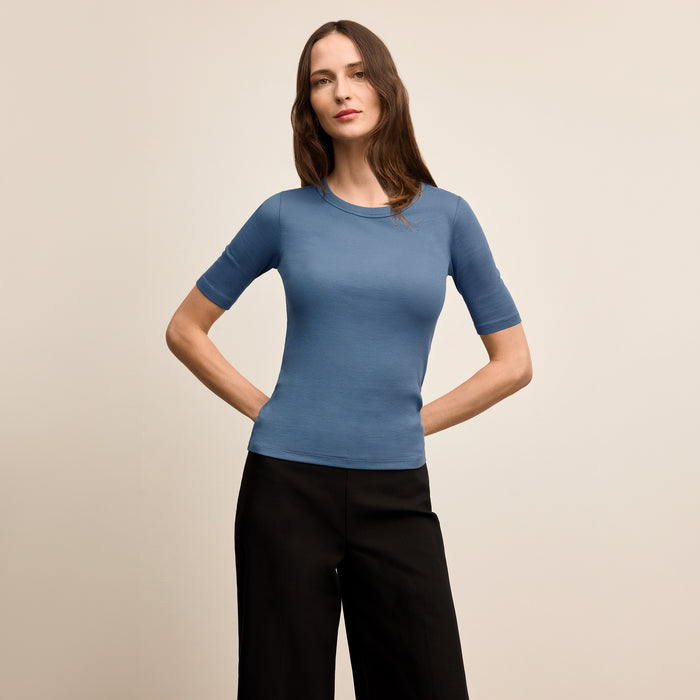 Woman wearing a blue short-sleeve top and black pants on a beige background | Lead