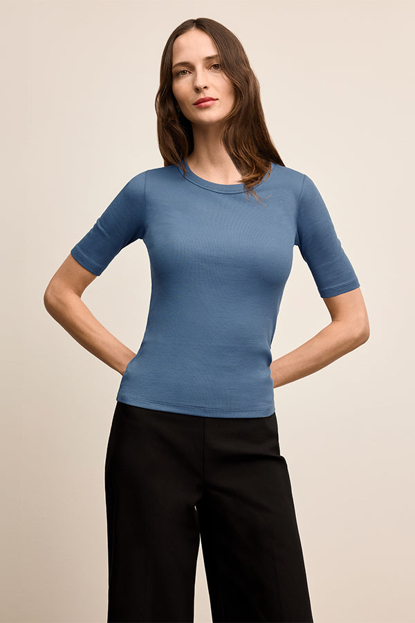 Woman wearing a blue short-sleeve top and black pants on a beige background | Exclude | Grid