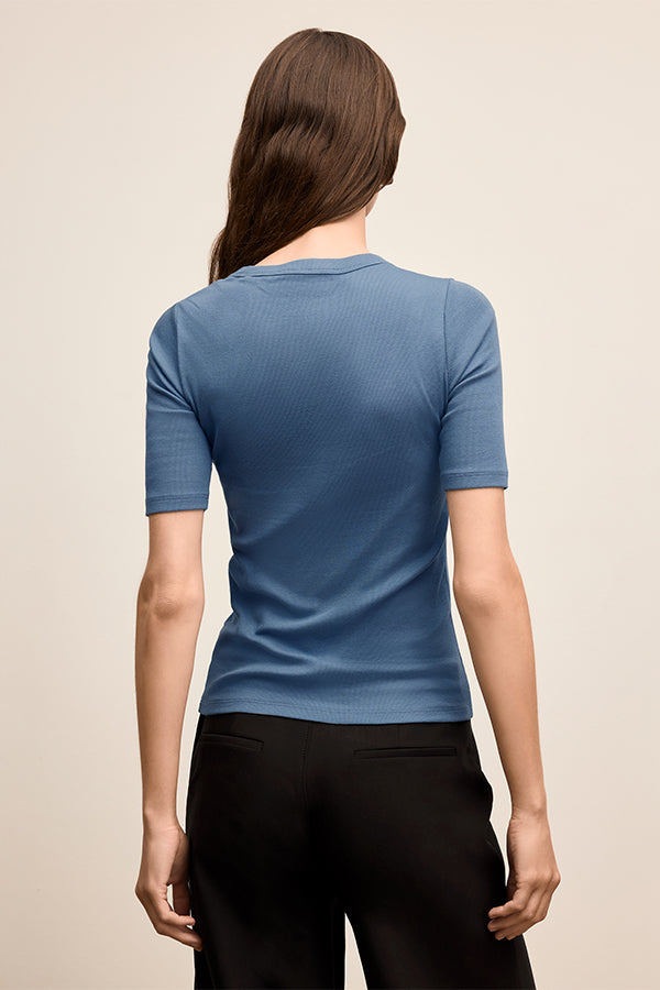 Woman wearing a blue short-sleeve shirt and black pants on a beige background | Exclude | Grid Hover