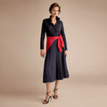 Woman wearing a black dress with a red sash on a beige background | Lead