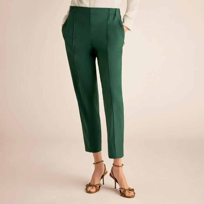 Green pants worn with a white top and gold sandals on a beige background | Lead