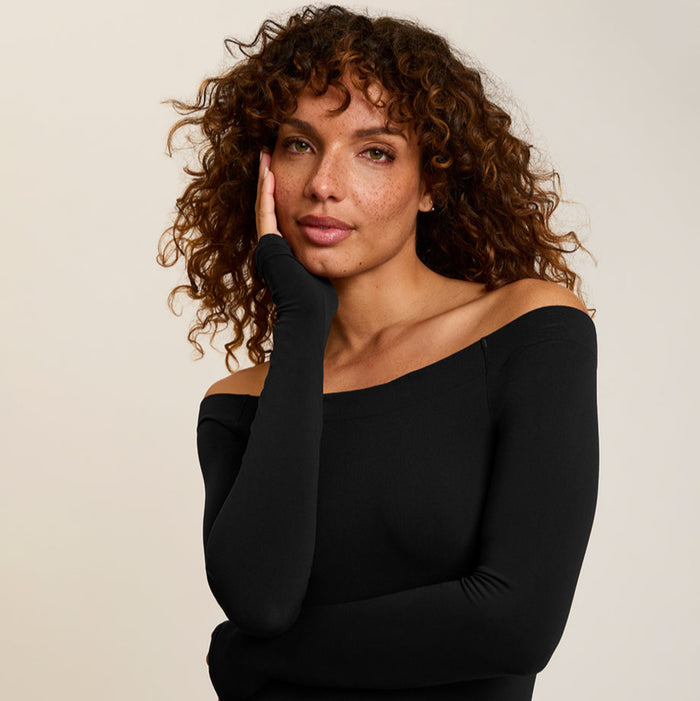 Woman wearing a black off-shoulder top against a beige background | Lead