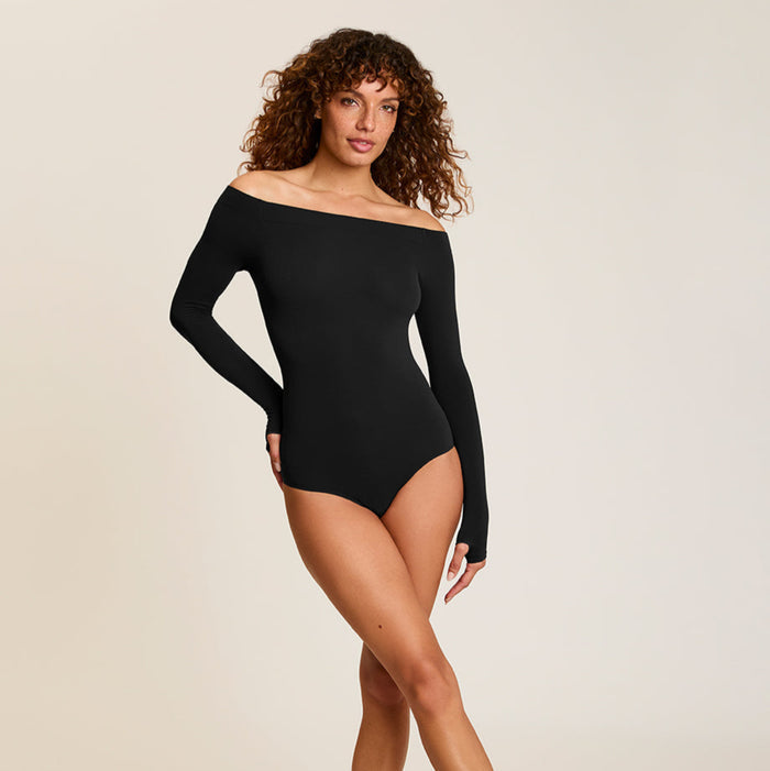 Woman wearing a black off-shoulder bodysuit on a plain background
