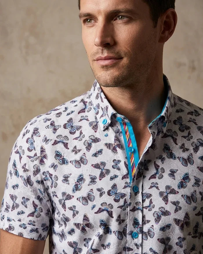 Man wearing a short-sleeve shirt with butterfly pattern against a neutral background