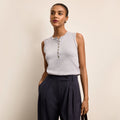 Woman wearing a light gray sleeveless top with buttons and dark blue pants against a beige background | Lead